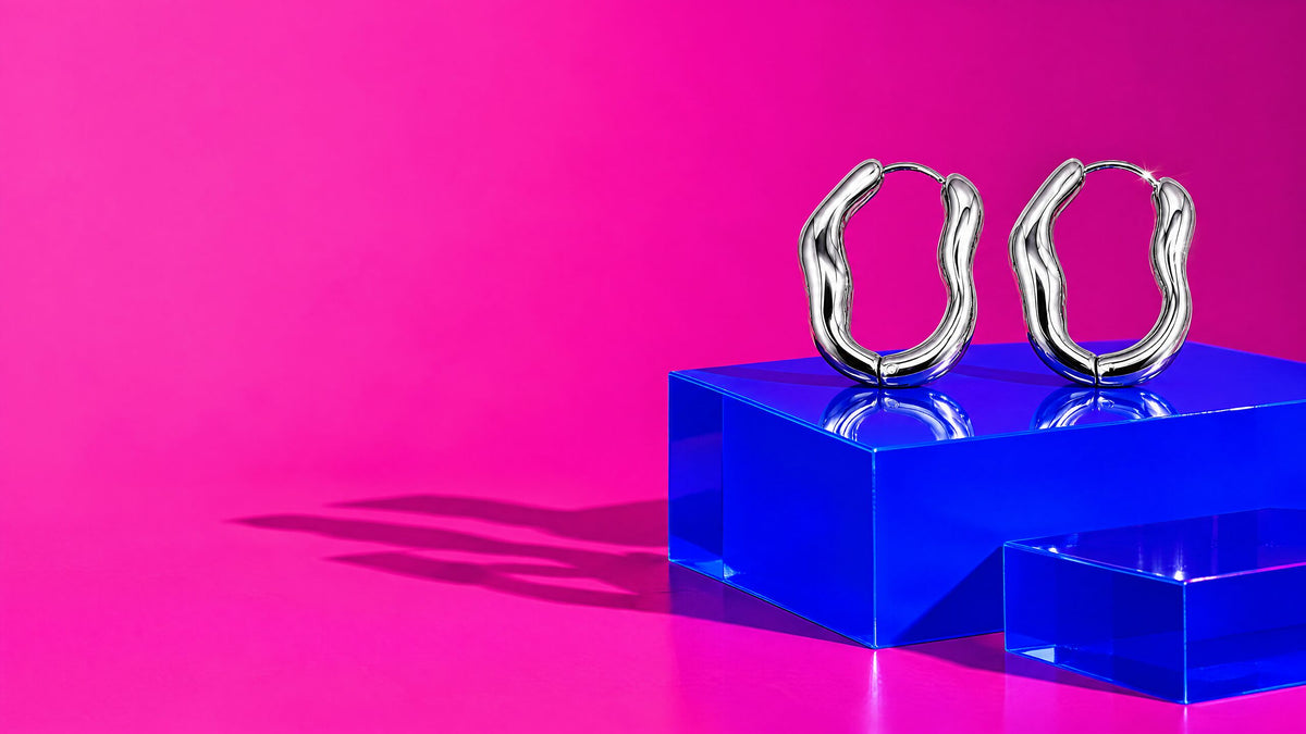 Orecchini a cerchio ondulati argento su un cubo blu cobalto lucido, fondo rosa acceso