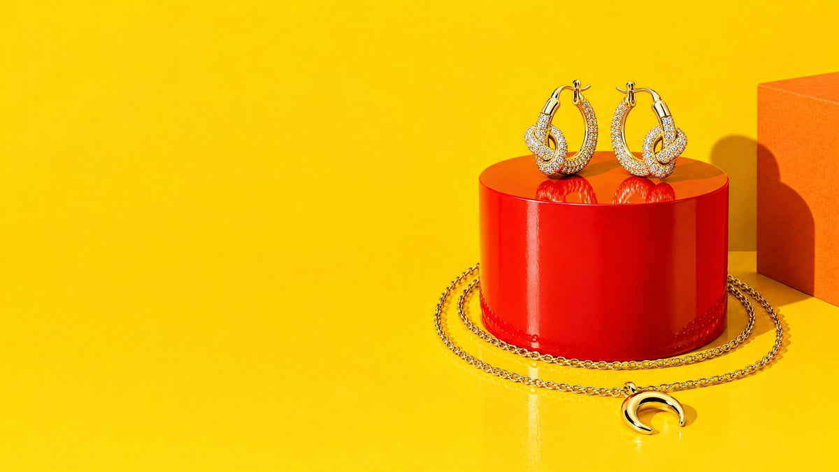 Orecchini nodo con zirconi su un cilindro rosso laccato e collana lunetta dorata, fondo giallo